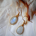 Boucles d'oreilles KAUMUDI Ginandger sur plumes blanches – détail des pierres de lune facettées à reflets bleus et crochet doré, boucles pendantes pierres naturelles Ginandger
