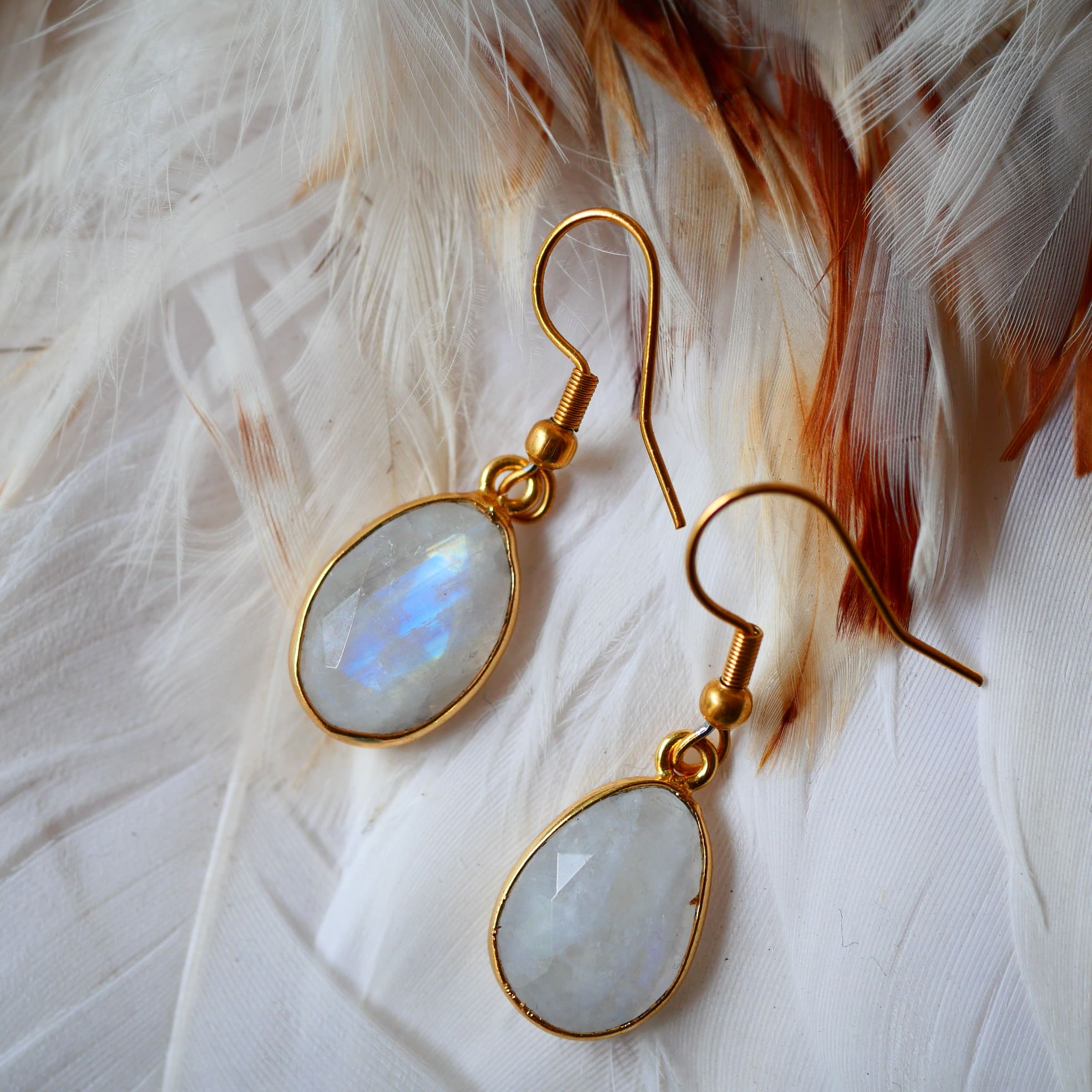 Boucles d'oreilles KAUMUDI Ginandger sur plumes blanches – détail des pierres de lune facettées à reflets bleus et crochet doré, boucles pendantes pierres naturelles Ginandger
