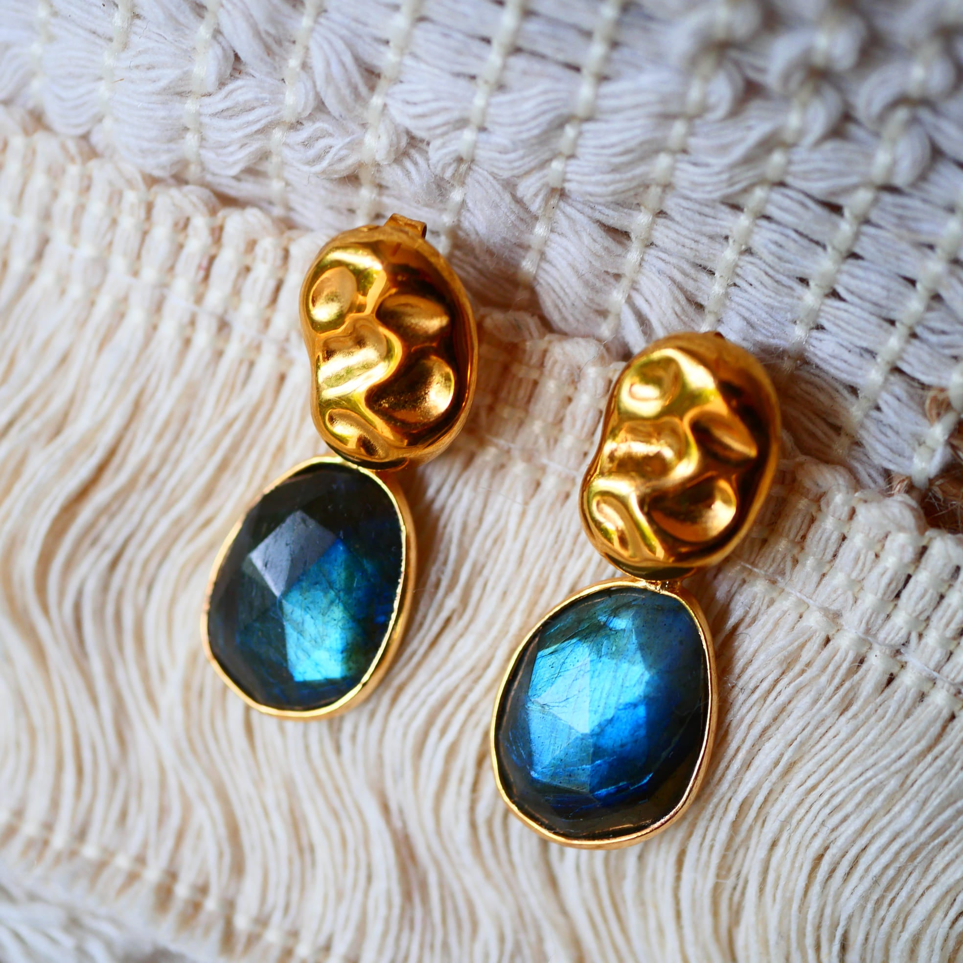 Boucles d'oreilles KAVACHA Ginandger posées sur macramé – labradorites bleues facettées serties or et puces dorées martelées ondulées, bijou pierres naturelles fait main à Paris
