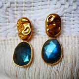 Boucles d'oreilles KAVACHA Ginandger portées au soleil en bord de mer – labradorite bleue irisée et puce dorée martelée, look été bijoux pierres naturelles
