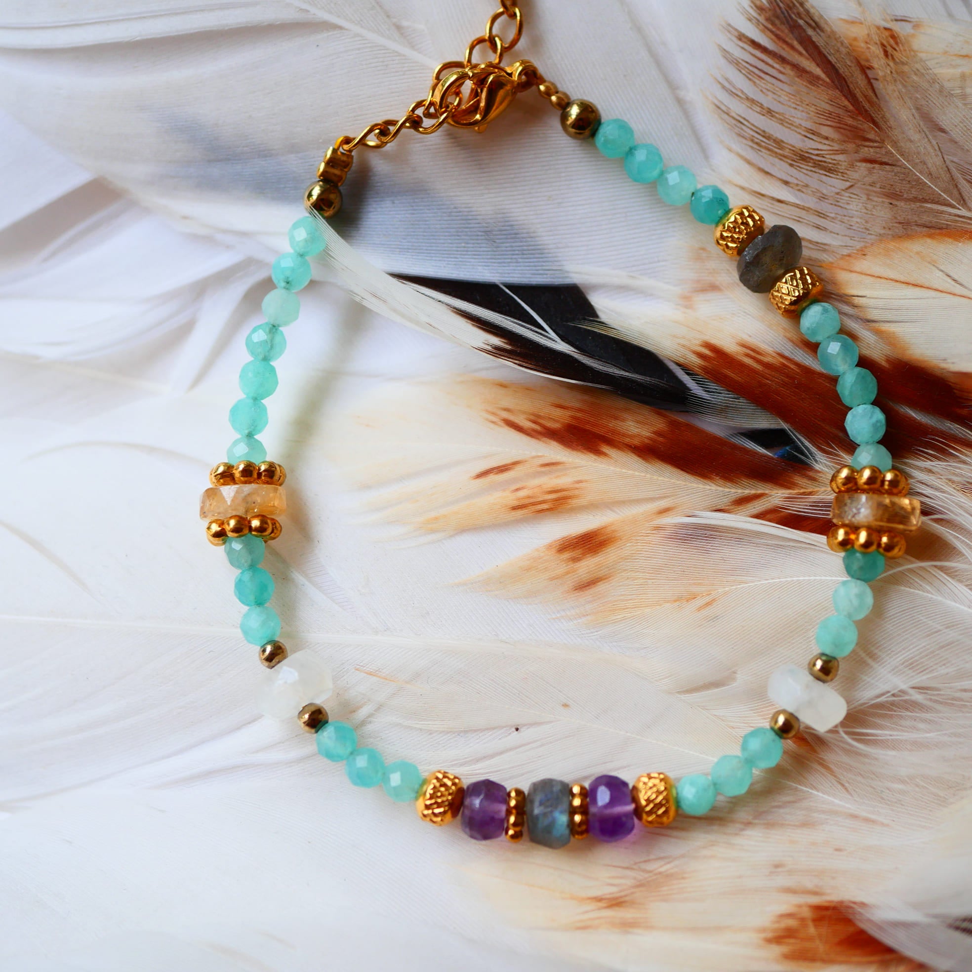 Bracelet LAKSHYA Ginandger posé sur plumes blanches – amazonites, améthystes, citrines et labradorites, perles dorées ciselées, bijou pierres naturelles fait main à Paris
