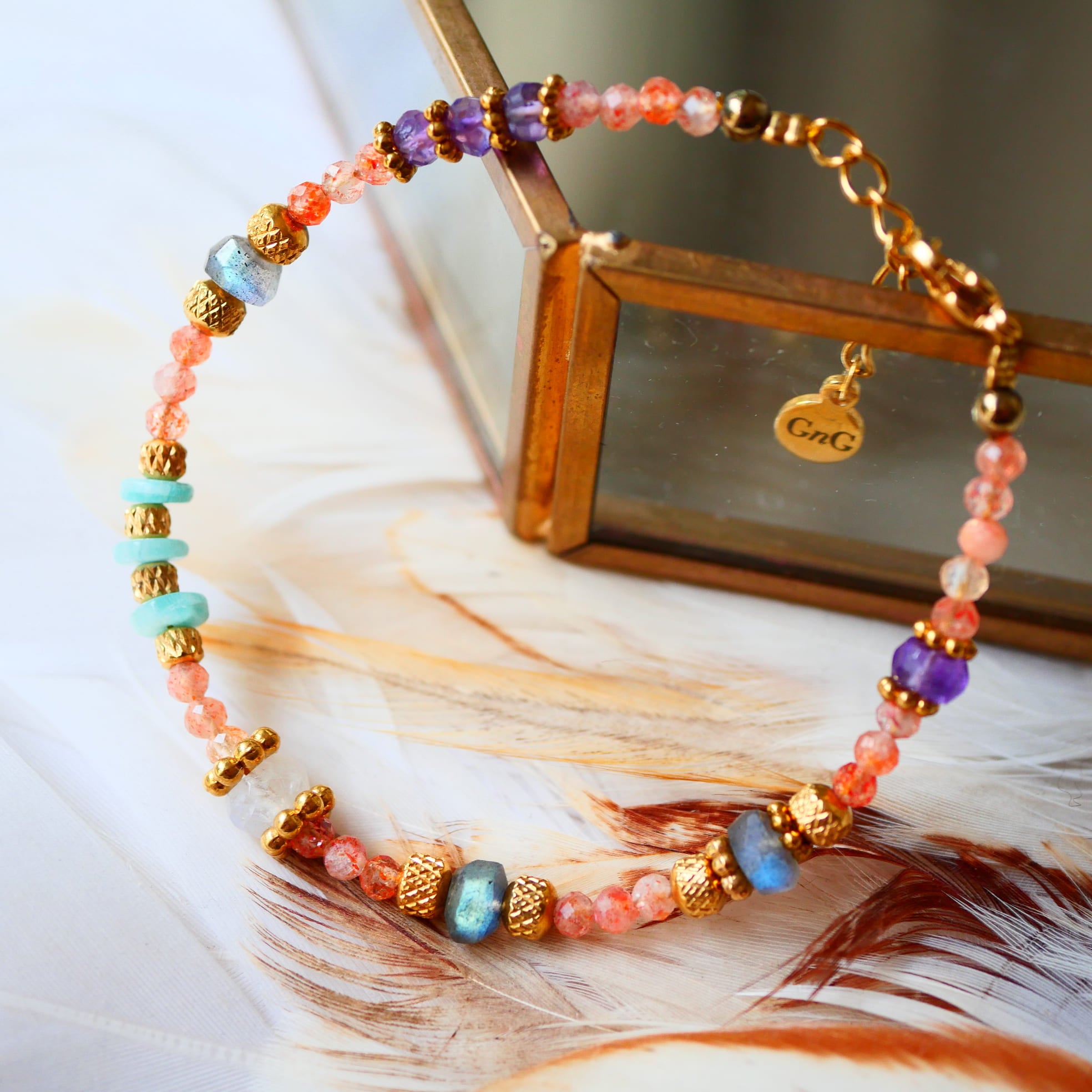 Bracelet SAMA Ginandger sur plumes et miroir doré – détail des pierres de soleil facettées, améthystes et labradorites, bracelet pierres naturelles Ginandger
