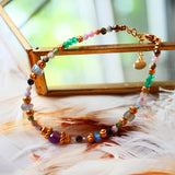 Bracelet THIRA Ginandger posé sur plumes et miroir doré – tourmalines multicolores, améthystes, labradorites et onyx verts, perles dorées, bijou pierres naturelles fait main à Paris
