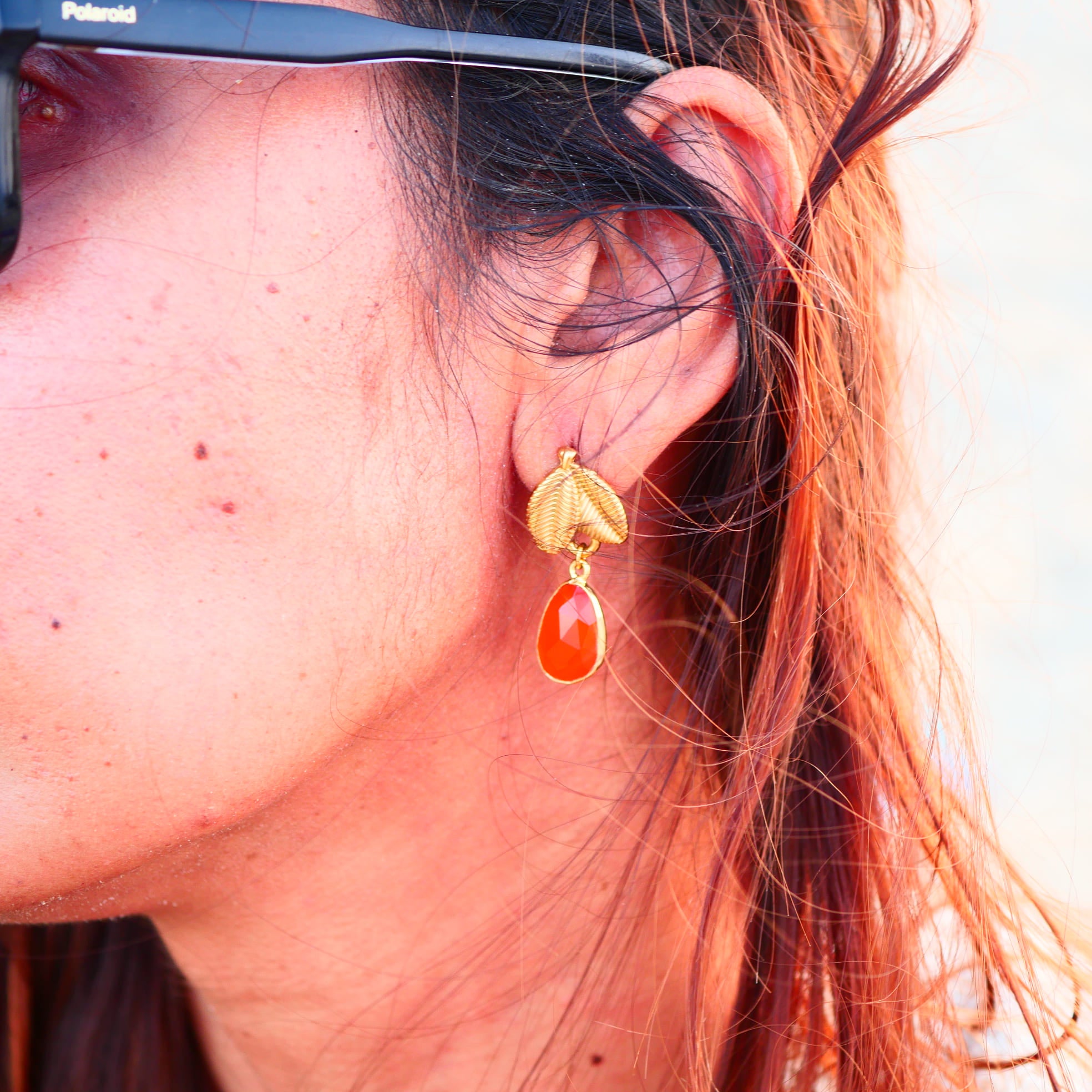 Boucles d'oreilles VEGA Ginandger portées au soleil – cornaline rouge-orangé facettée et puce feuille dorée texturée, look été bijoux pierres naturelles
