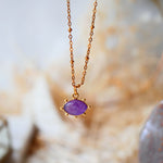 Collier AJNA Ginandger améthyste - pendentif œil sculpté violet serti or, suspendu sur fond de cristal
