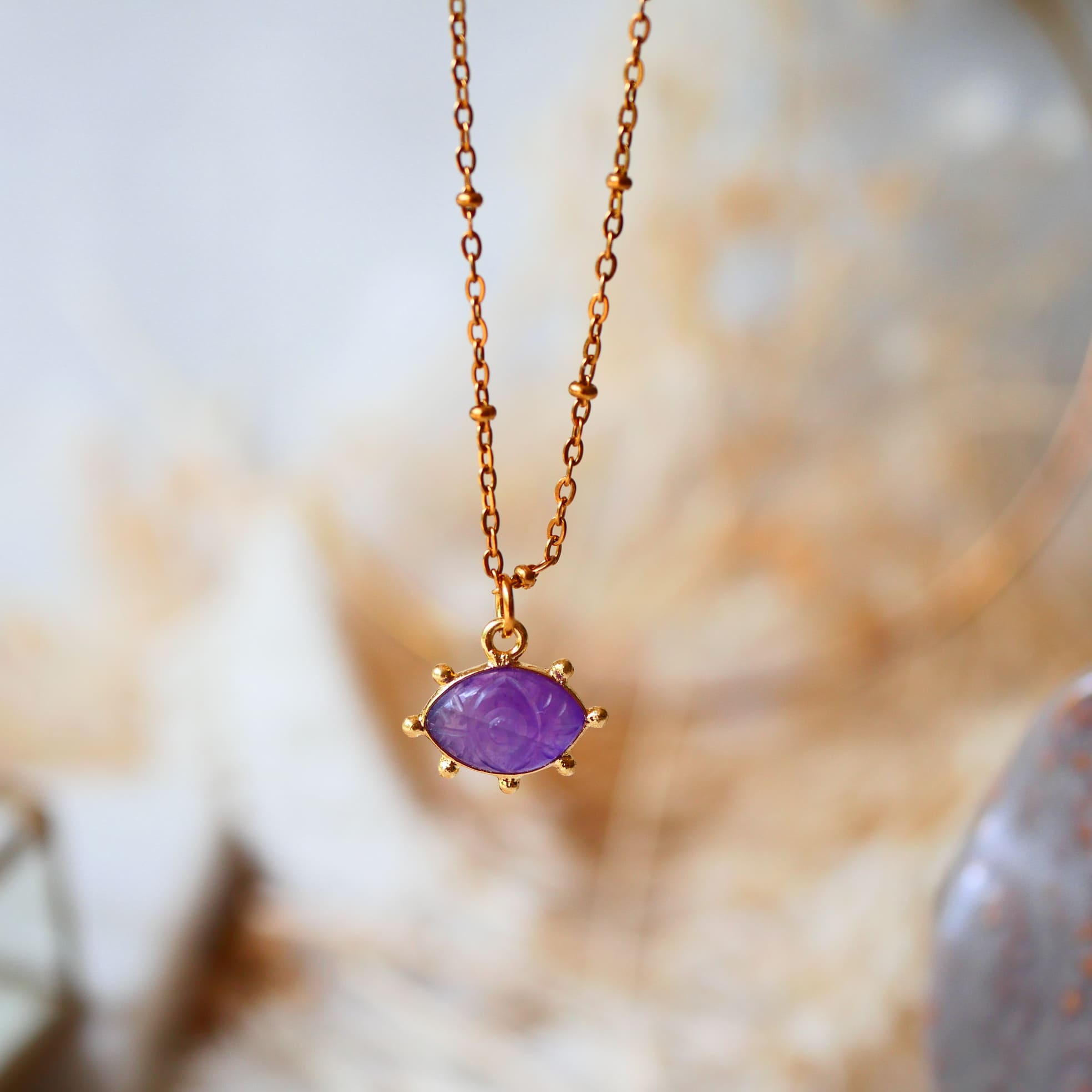 Collier AJNA Ginandger améthyste - pendentif œil sculpté violet serti or, suspendu sur fond de cristal
