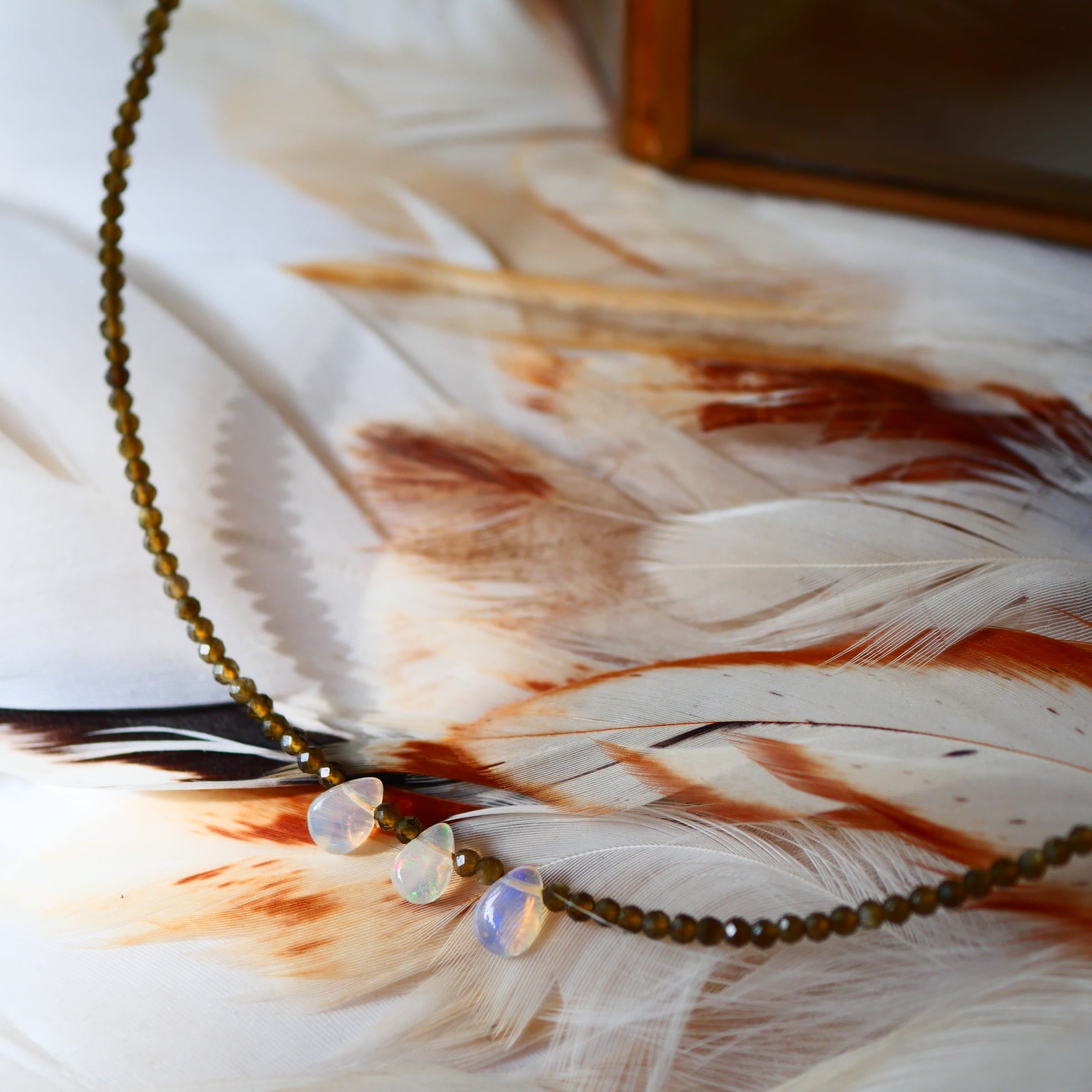 Collier ANTARA Ginandger - perles d'obsidienne facettées et pendentifs opales nacrées sur fond de plumes
