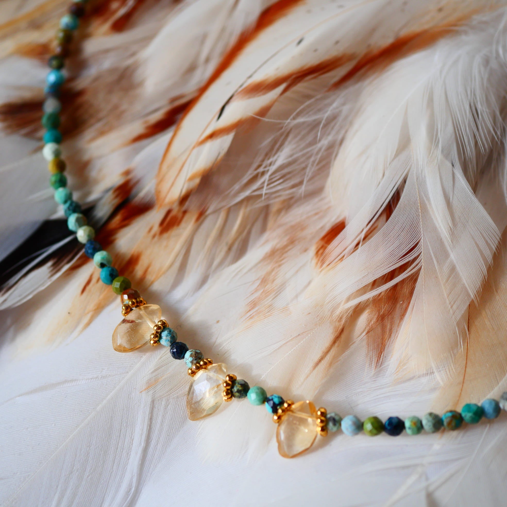 Collier DEEPTI Ginandger - détail gouttes de citrine dorée sur perles de turquoise multicolores, fond plumes

