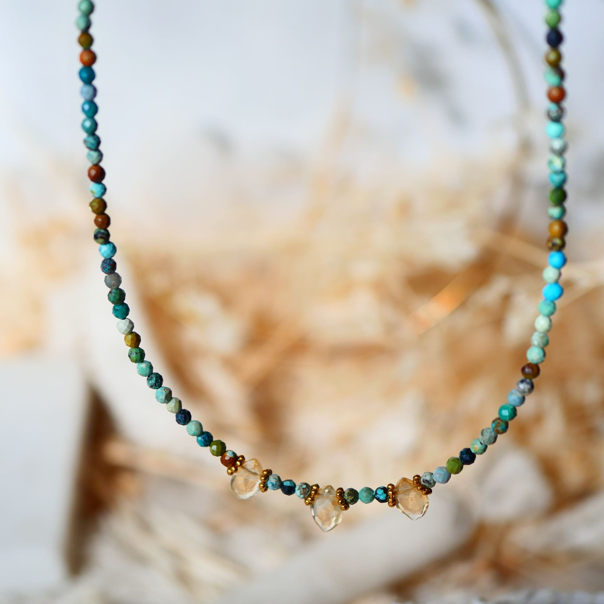 Collier DEEPTI Ginandger suspendu - perles de turquoise facettées et gouttes de citrine, fond floral naturel
