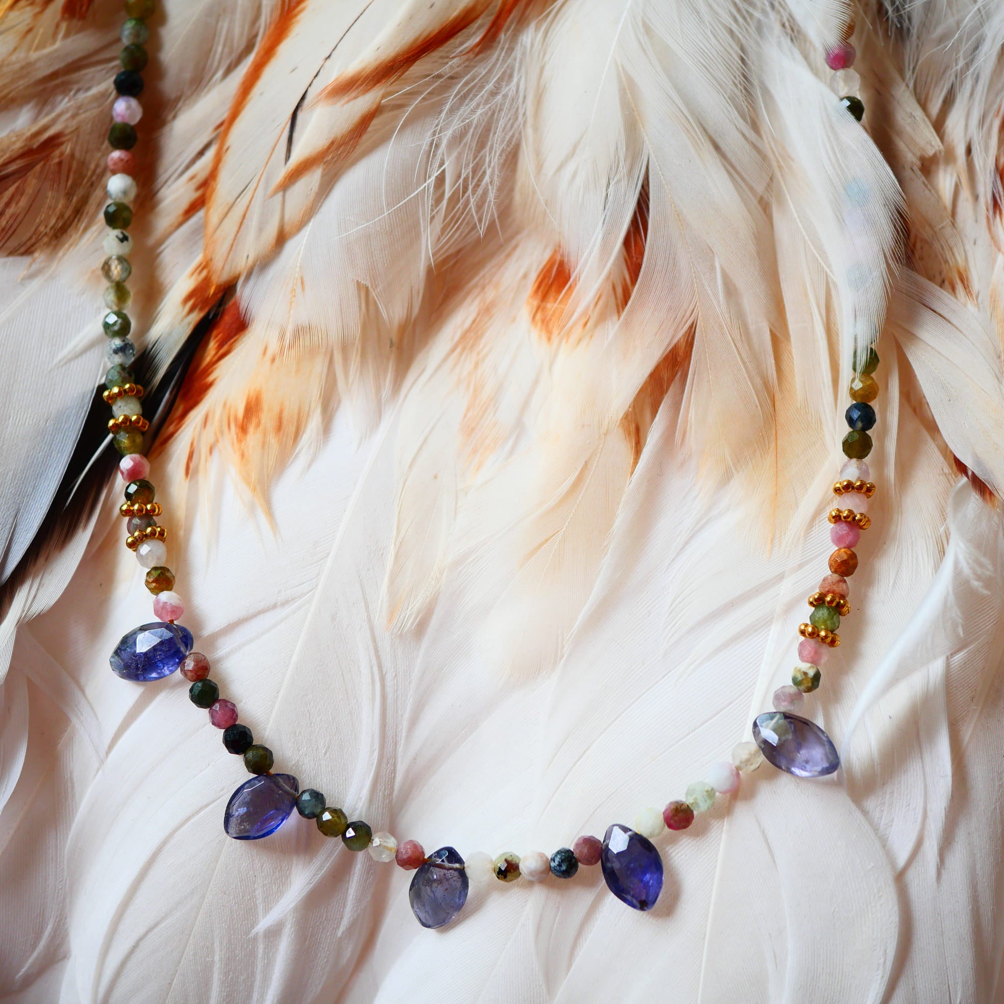 Collier RANGA Ginandger - tourmalines multicolores et iolites facettées sur fond de plumes blanches
