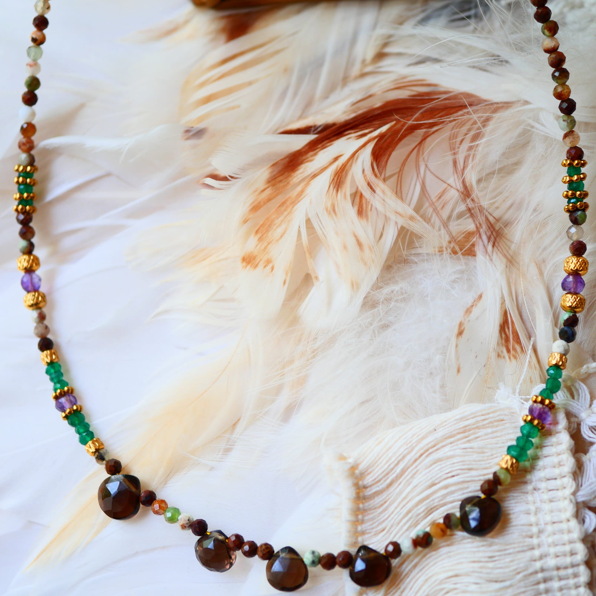 Collier VRIKSHA Ginandger posé sur plumes blanches – chrysoprase, onyx vert, améthyste et quartz fumé, breloques dorées, bijou pierres naturelles fait main à Paris
